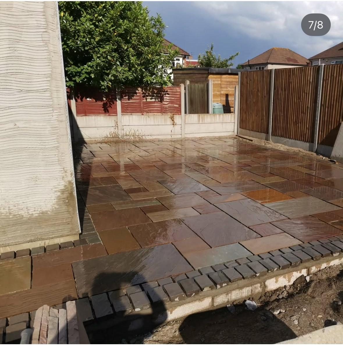 Completed natural stone style paved patio with brick edging and timber fencing